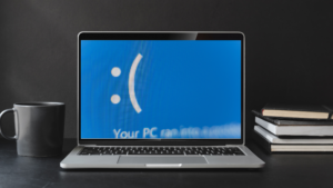 scene of a desk with coffee mug laptop and books. the laptop is suggesting a frozen computer screen