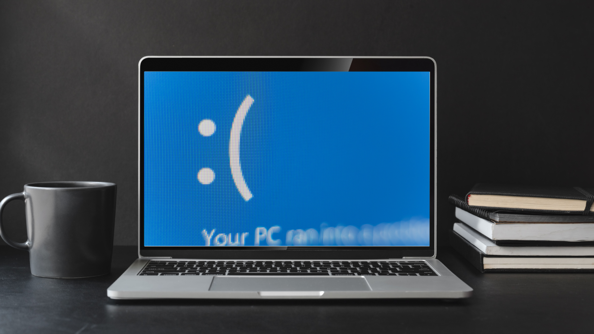 scene of a desk with coffee mug laptop and books. the laptop is suggesting a frozen computer screen