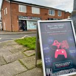 outside a board sign showing the beat the expert event with cache4 shop in the background