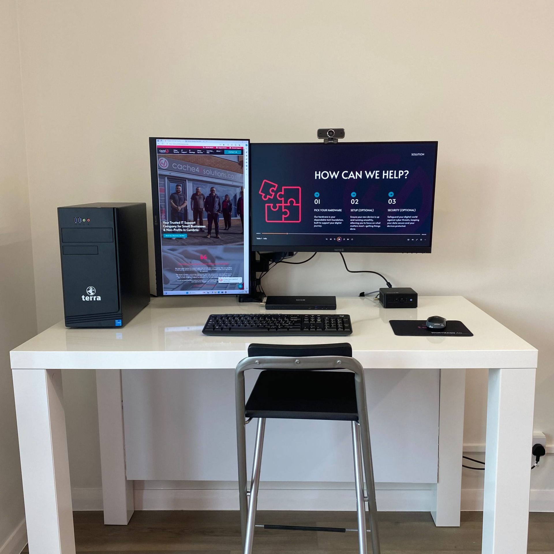This image shows a clean, professional workstation setup featuring dual monitors (one vertical and one horizontal), a Terra desktop PC, a keyboard, a mouse, and a webcam on a minimalist white desk. The setup emphasizes productivity and a sleek design, suitable for a business or IT environment.