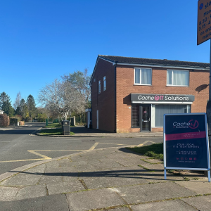 a sign on a street corner with the Cache4 shop building behind. Blue sky